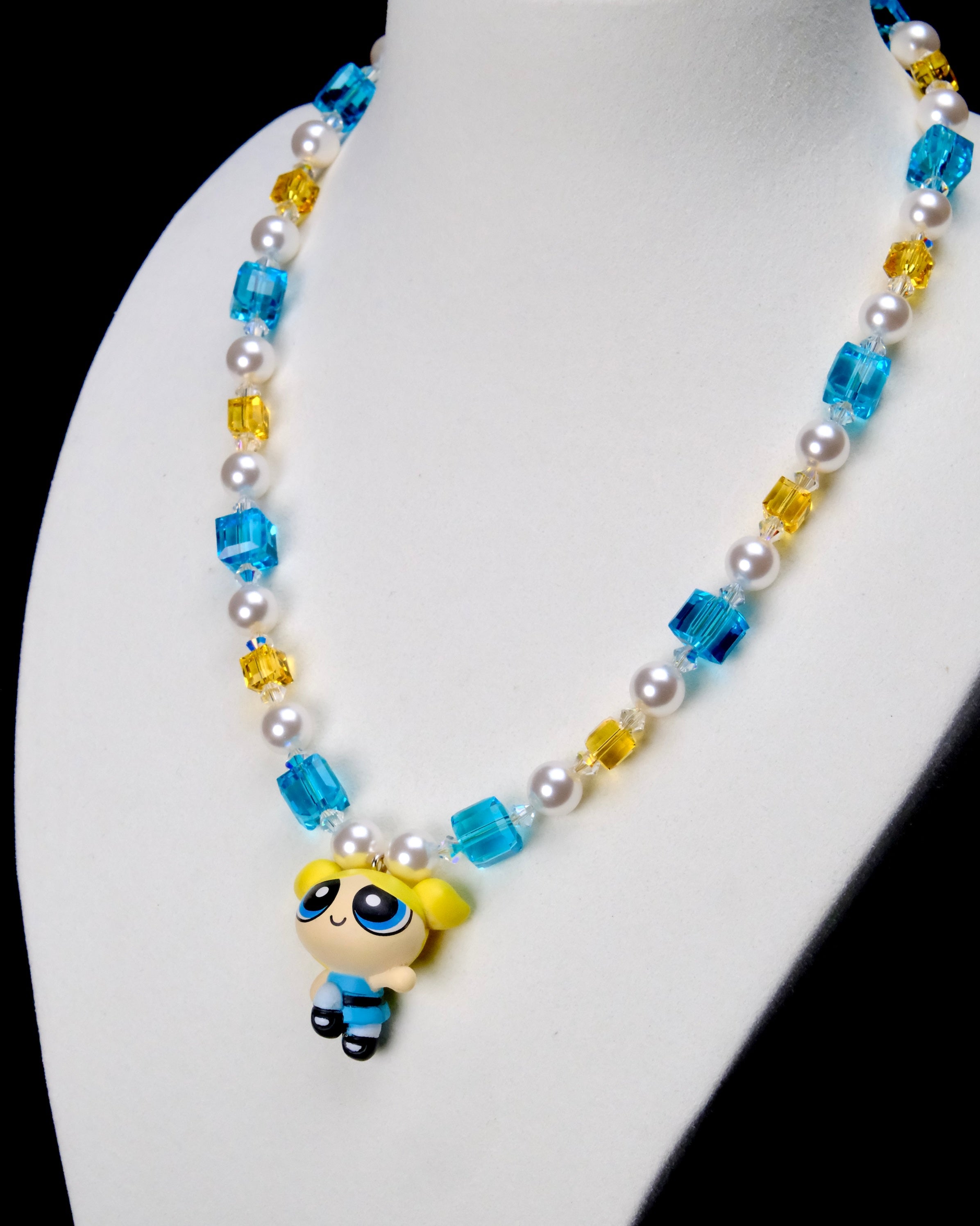 Angled close-up of Blue Dreamer Charm Necklace showing the blue-outfit girl pendant, aqua crystals and white pearls.