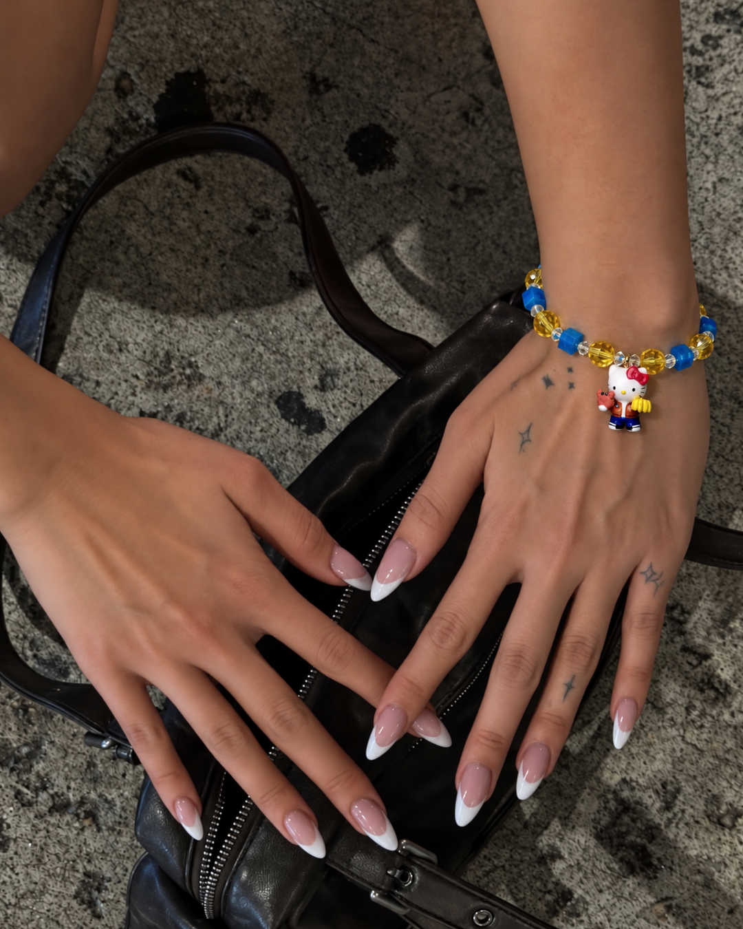Blue & Gold Playday Cat Charm Bracelet with blue cubes, golden beads and a cat pendant, worn on a wrist above a black handbag.