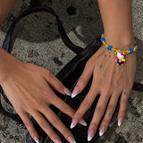 Blue & Gold Playday Cat Charm Bracelet with blue cubes, golden beads and a cat pendant, worn on a wrist above a black handbag.