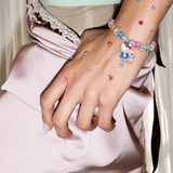 Rainbow crystal bracelet with two white character charms on a gem-decorated wrist, styled against pale pink satin.