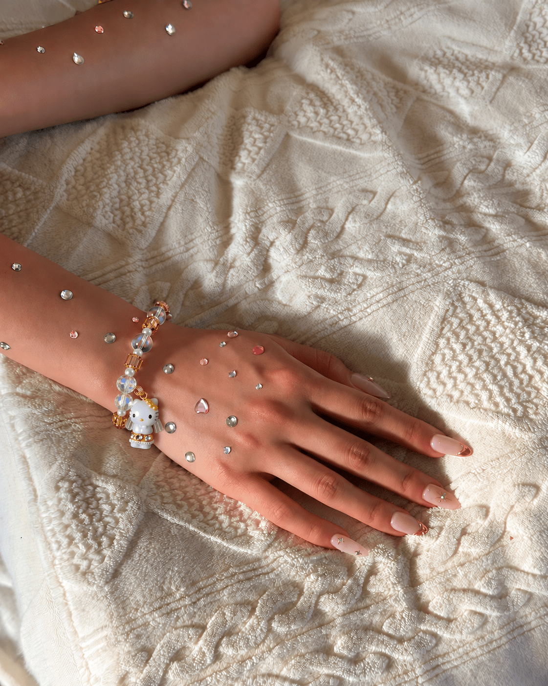 Champagne and iridescent crystal bracelet with a winged cat charm worn on a wrist decorated with colorful rhinestones.