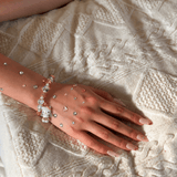 Champagne and iridescent crystal bracelet with a winged cat charm worn on a wrist decorated with colorful rhinestones.