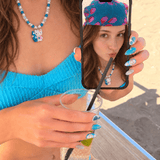 Blue crystal and pearl cat charm necklace worn with a turquoise top, shown beside a phone displaying the same necklace.