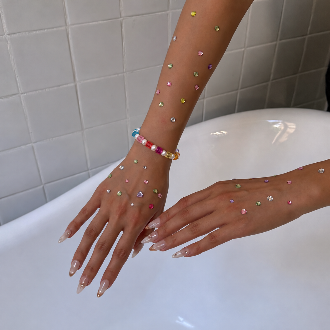 Rainbow crystal cube and pearl bracelet worn on a wrist above a bathtub, with colorful rhinestones decorating the hands.