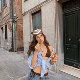 Model wearing a blue pearl and crystal mermaid cat necklace with a striped shirt, holding a cup of fruit on a stone street.
