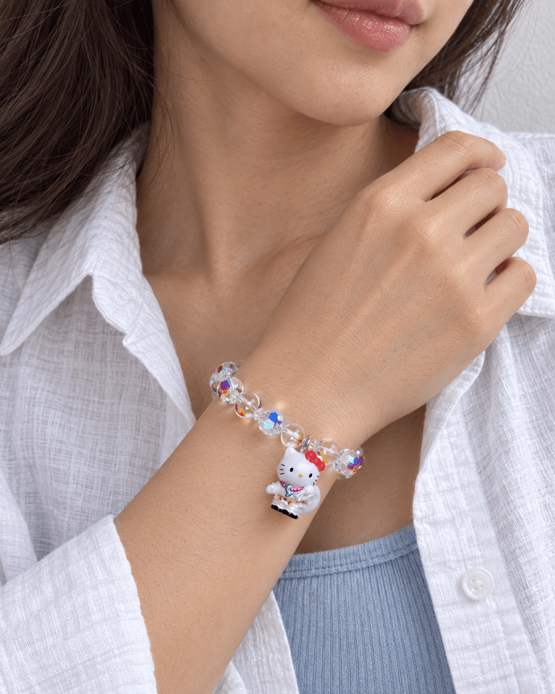 Woman in a white shirt wearing an iridescent crystal bracelet with a white cat charm.