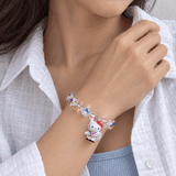 Woman in a white shirt wearing an iridescent crystal bracelet with a white cat charm.