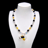 Black crystal cubes, yellow crystal rounds and white pearl beads frame a Donald Duck charm in a dark outfit, holding a gold-colored musical instrument.