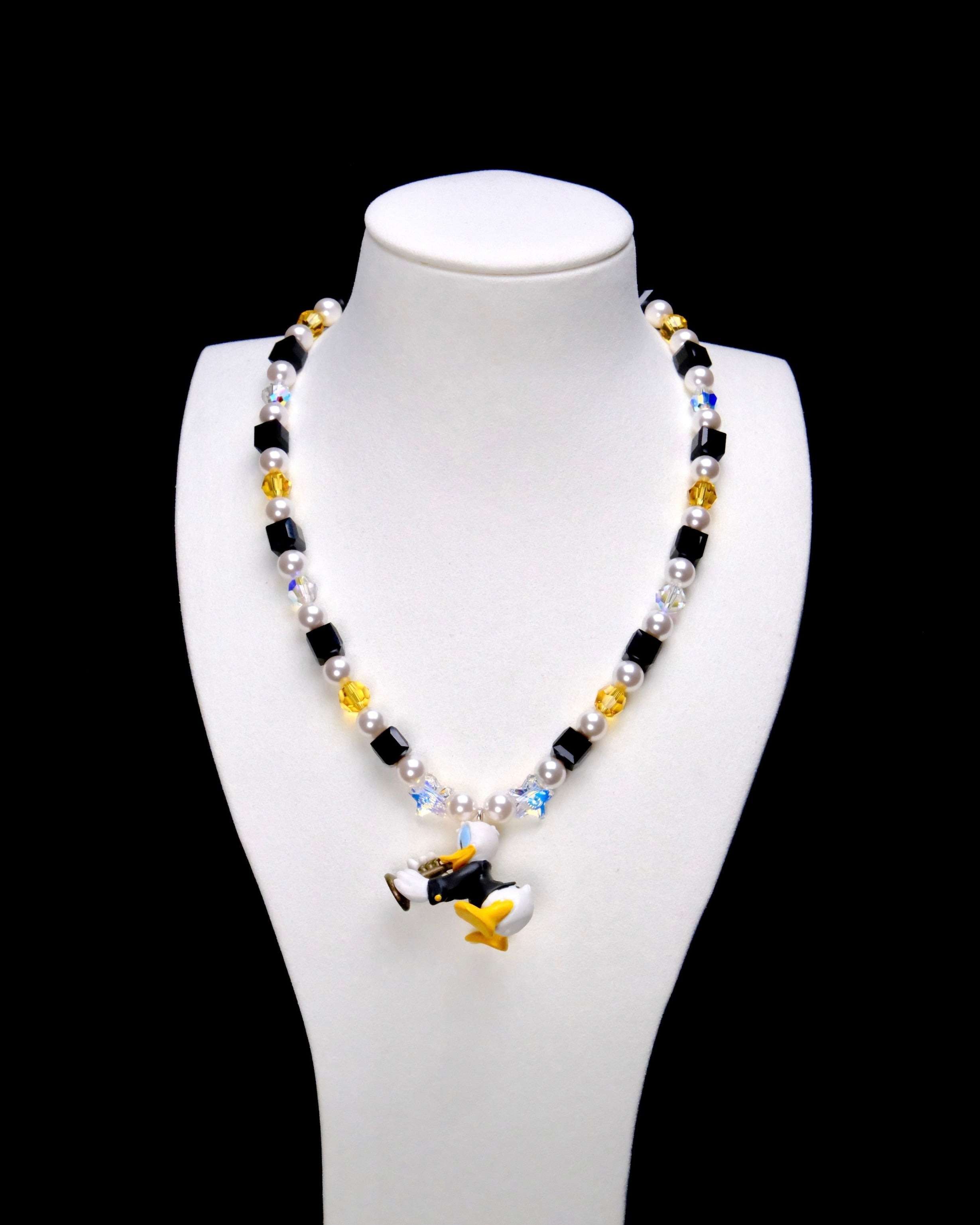 Black crystal cubes, yellow crystal rounds and white pearl beads frame a Donald Duck charm in a dark outfit, holding a gold-colored musical instrument.
