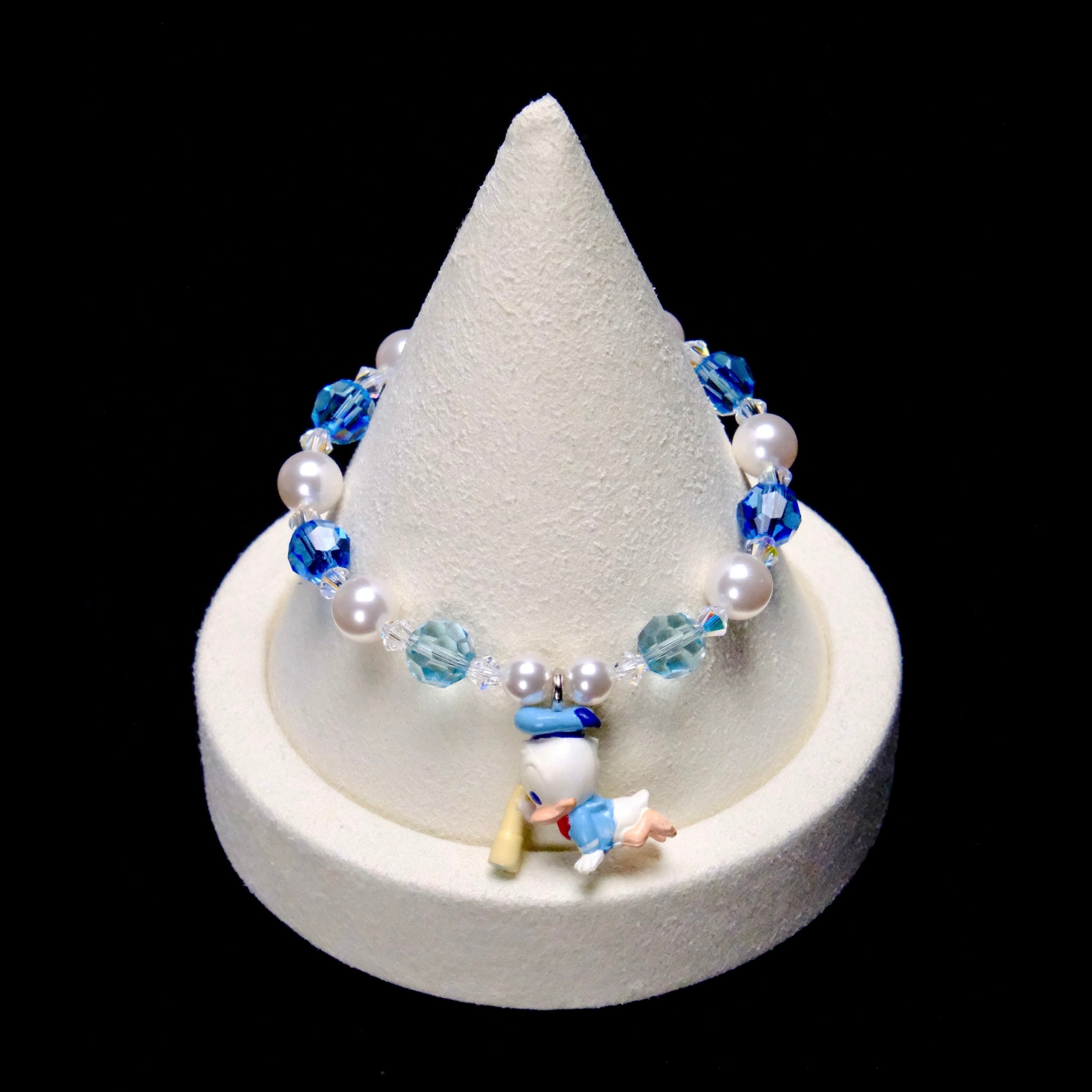Deep blue and pale aqua crystal rounds alternate with white pearl beads and clear spacers, framing a little Donald Duck charm in a light blue sailor outfit.