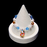 Blue and amber crystal rounds alternate with white pearl beads. Pluto sits at the center wearing a blue cap and a red-and-white life ring.