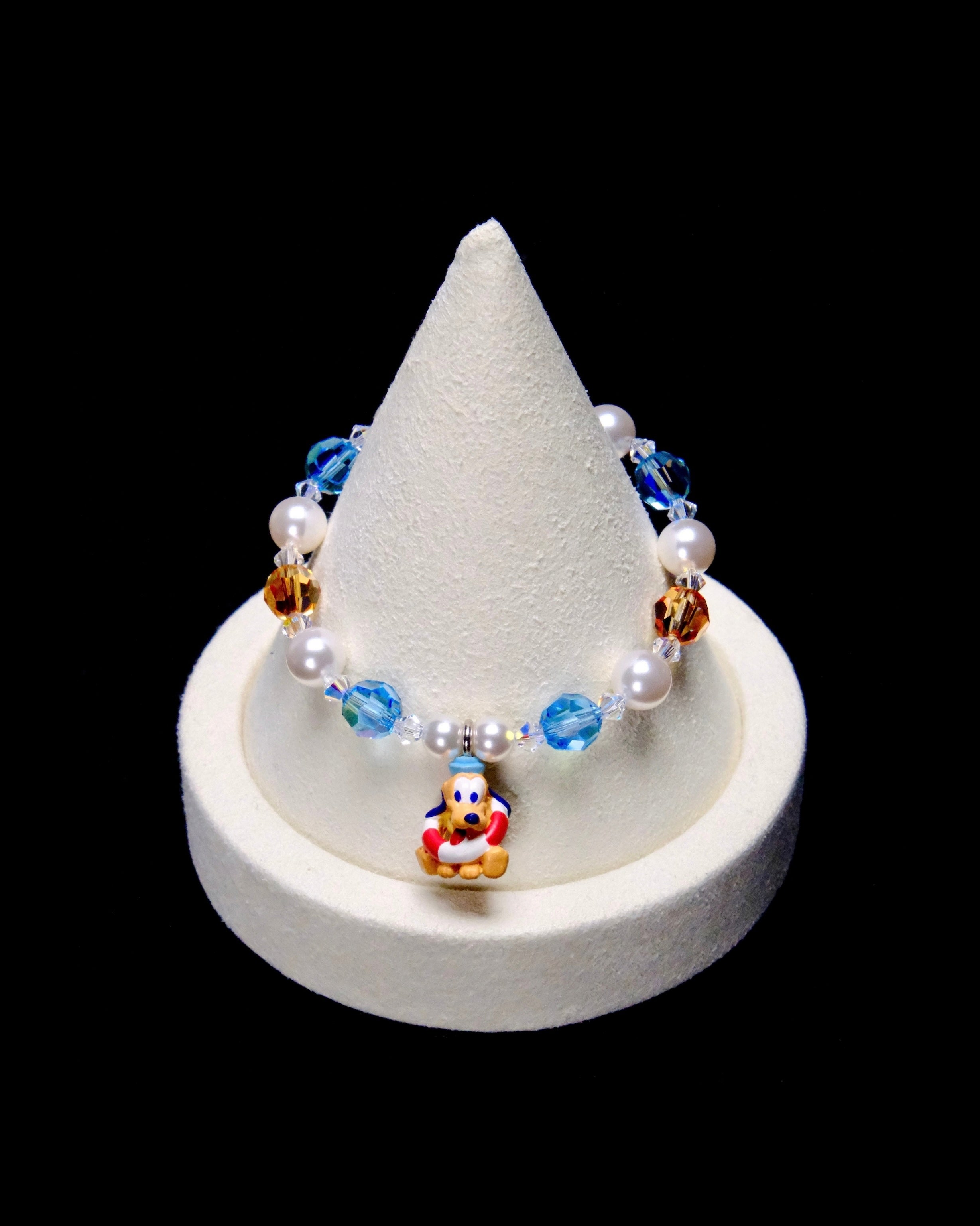Blue and amber crystal rounds alternate with white pearl beads. Pluto sits at the center wearing a blue cap and a red-and-white life ring.