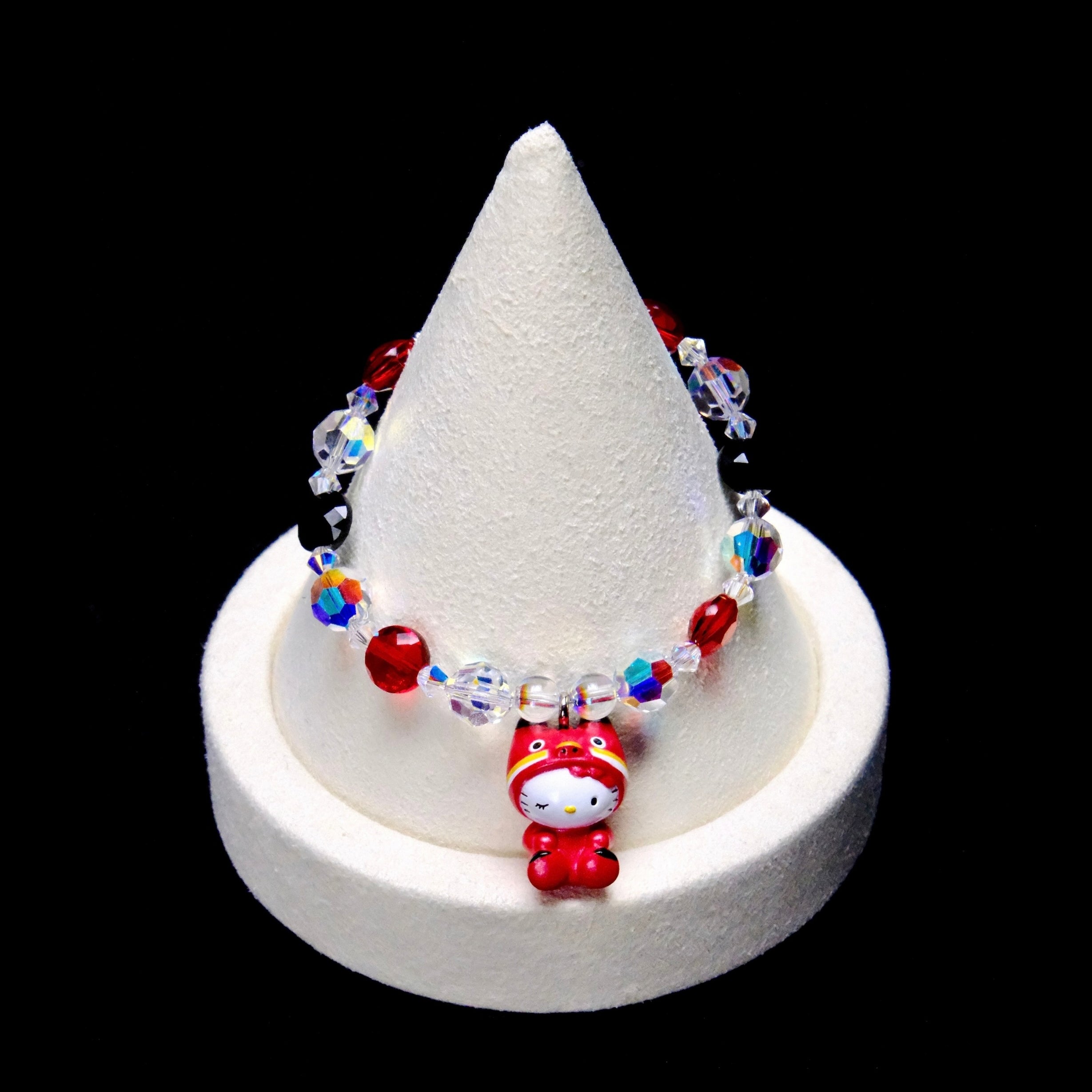Red, black and clear iridescent crystal beads frame a Hello Kitty charm with closed eyes, wearing a bright red animal costume.