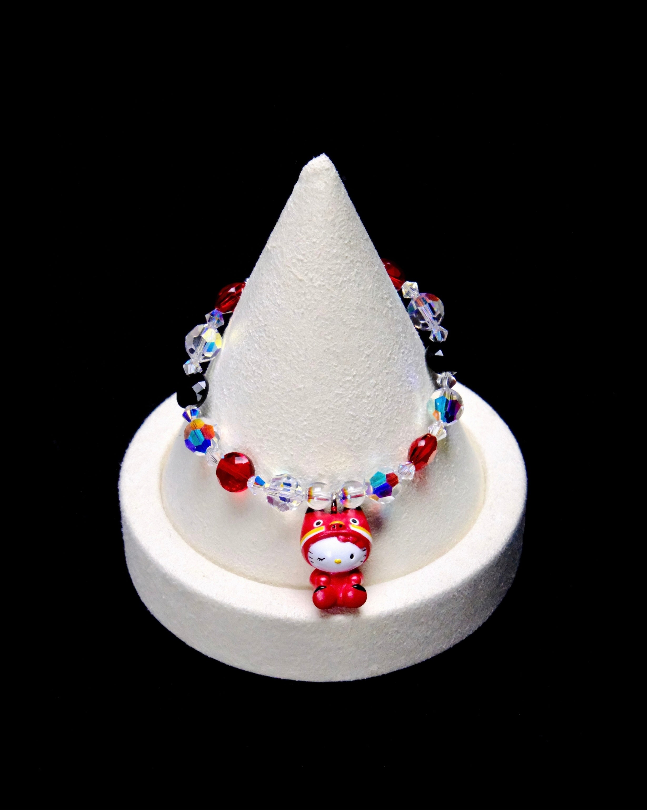 Red, black and clear iridescent crystal beads frame a Hello Kitty charm with closed eyes, wearing a bright red animal costume.