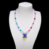 Blue and pink crystal rounds with clear iridescent beads and two larger clear crystals frame a Stitch charm wearing a pink bow, blue top and yellow skirt.