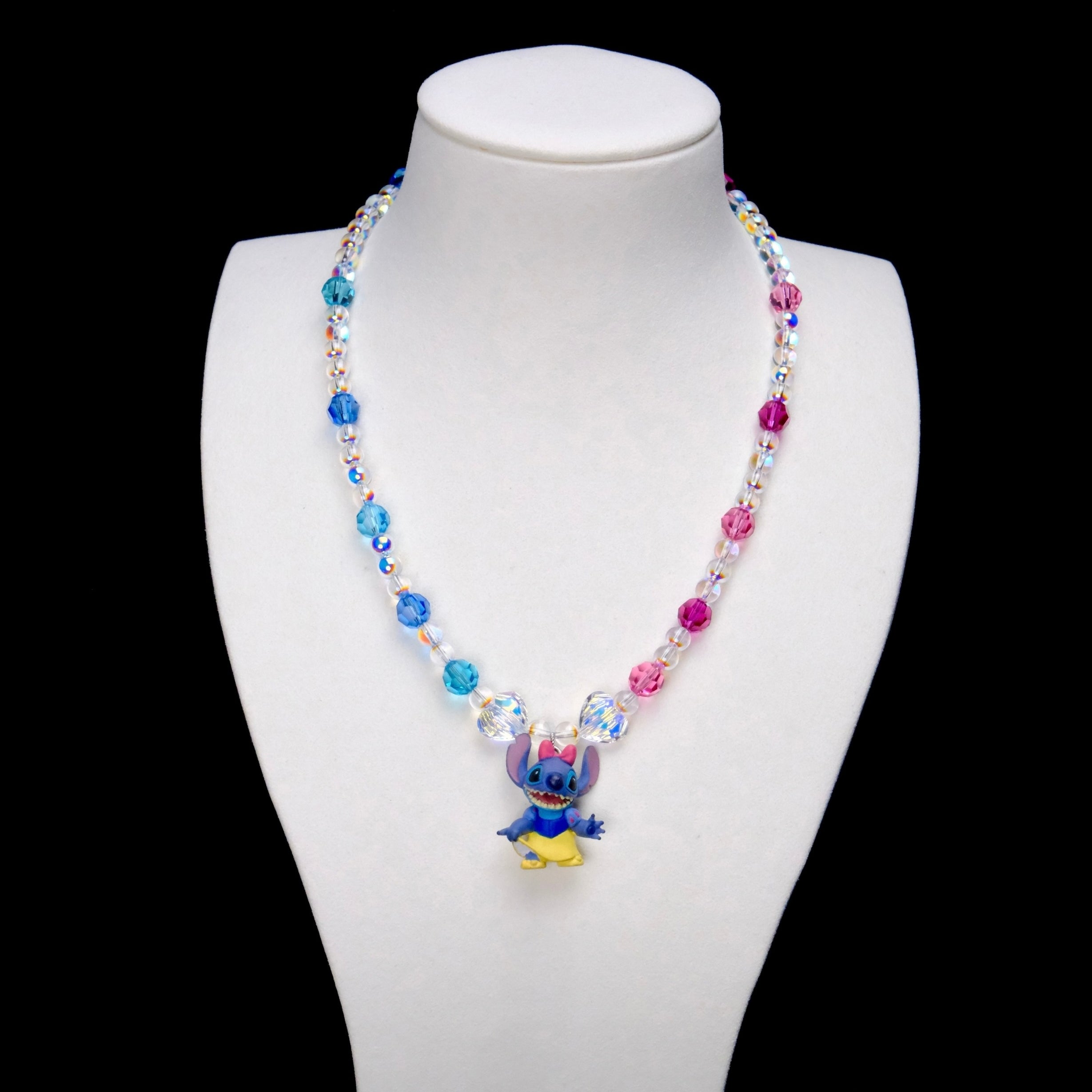Blue and pink crystal rounds with clear iridescent beads and two larger clear crystals frame a Stitch charm wearing a pink bow, blue top and yellow skirt.