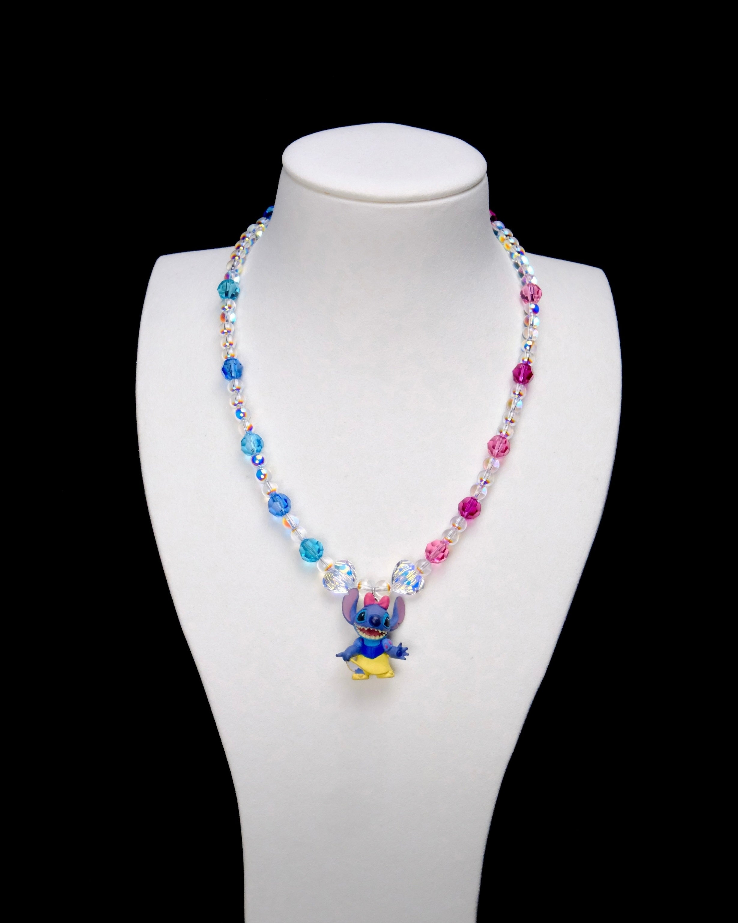Blue and pink crystal rounds with clear iridescent beads and two larger clear crystals frame a Stitch charm wearing a pink bow, blue top and yellow skirt.