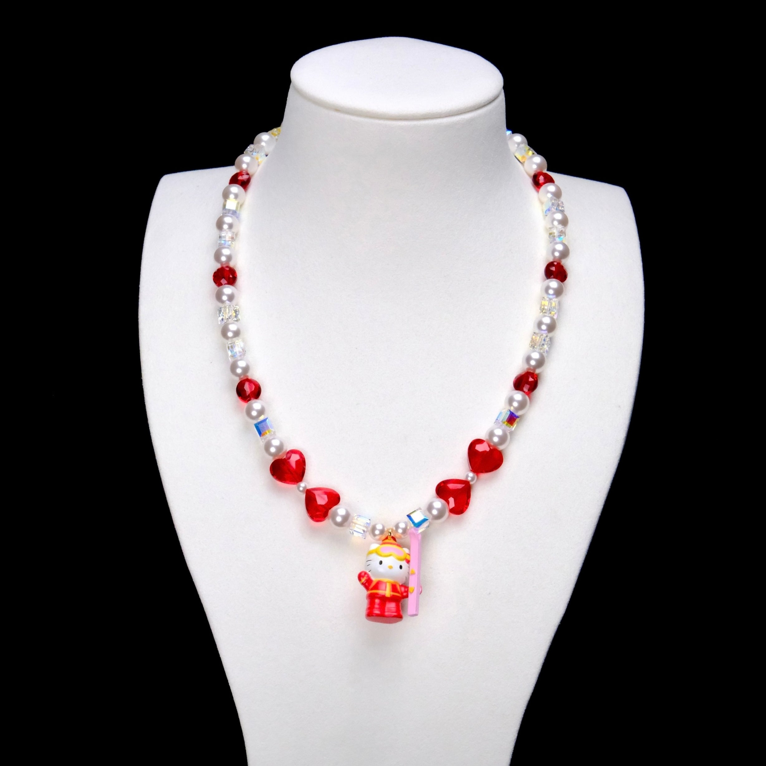 Red crystal rounds and four red hearts pair with white pearl beads and iridescent crystal cubes. A Hello Kitty charm in a red winter outfit holds a pink board.