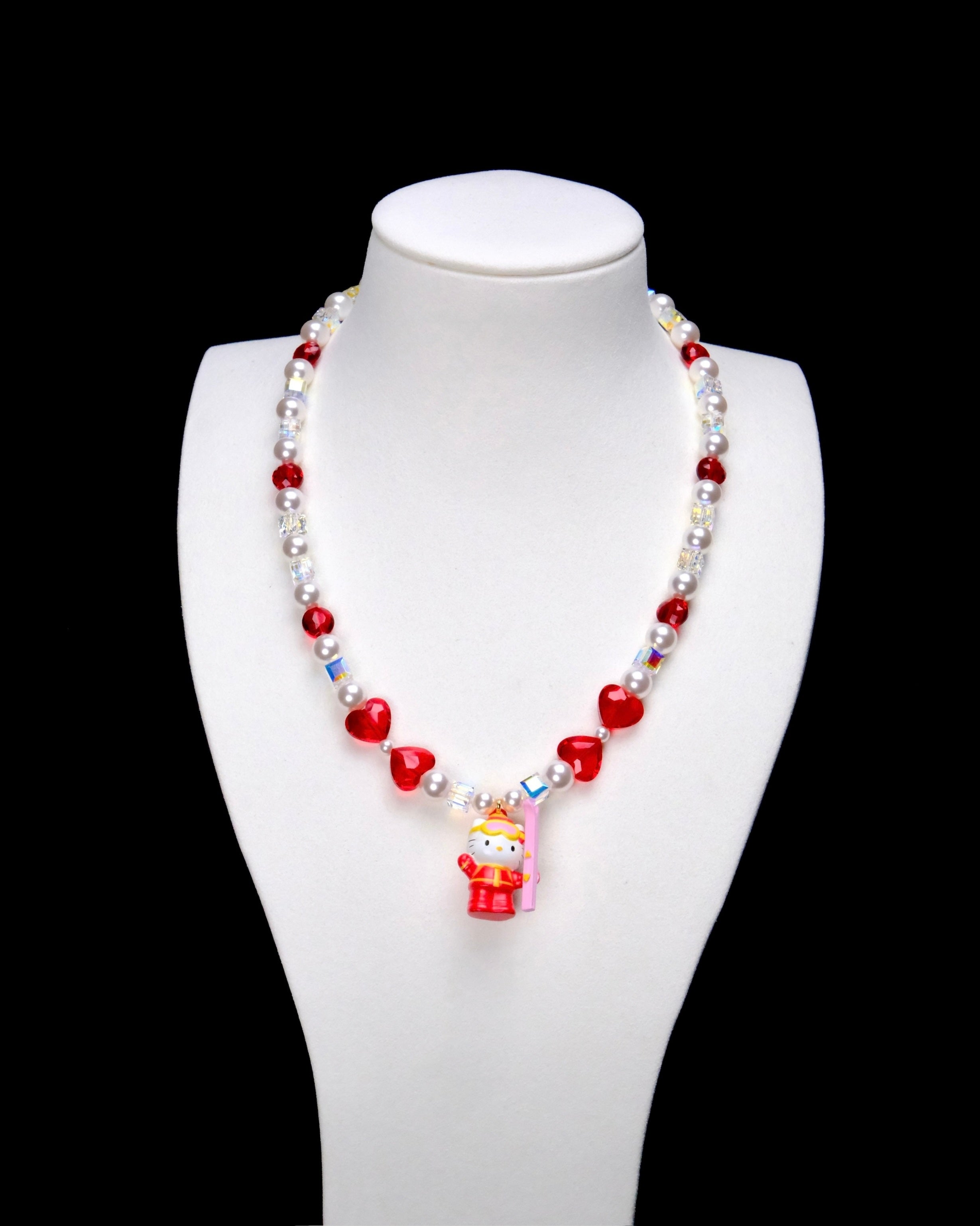 Red crystal rounds and four red hearts pair with white pearl beads and iridescent crystal cubes. A Hello Kitty charm in a red winter outfit holds a pink board.