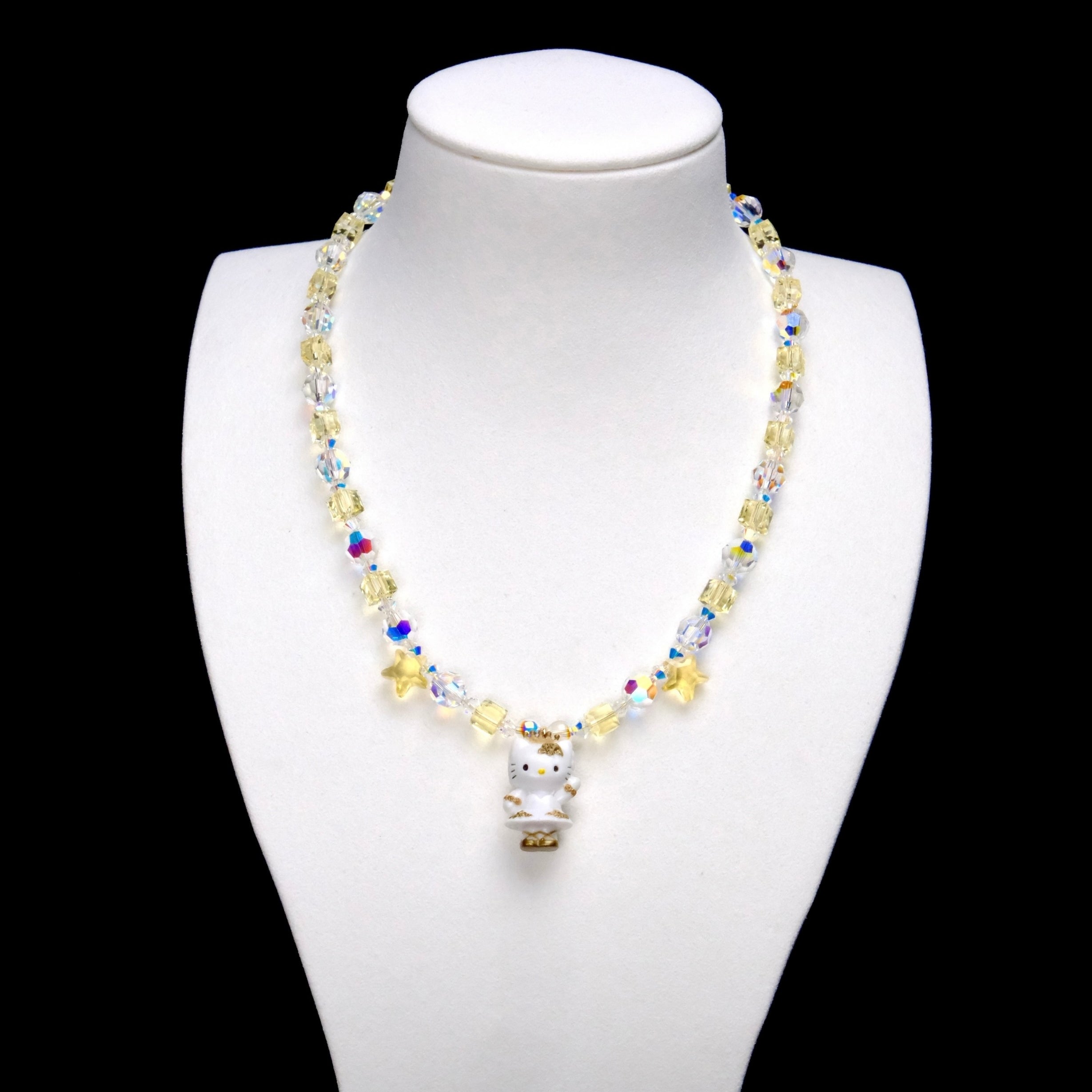 Pale yellow crystal cubes alternate with clear iridescent rounds. Two yellow stars frame a Hello Kitty charm in a white outfit with gold-colored details.
