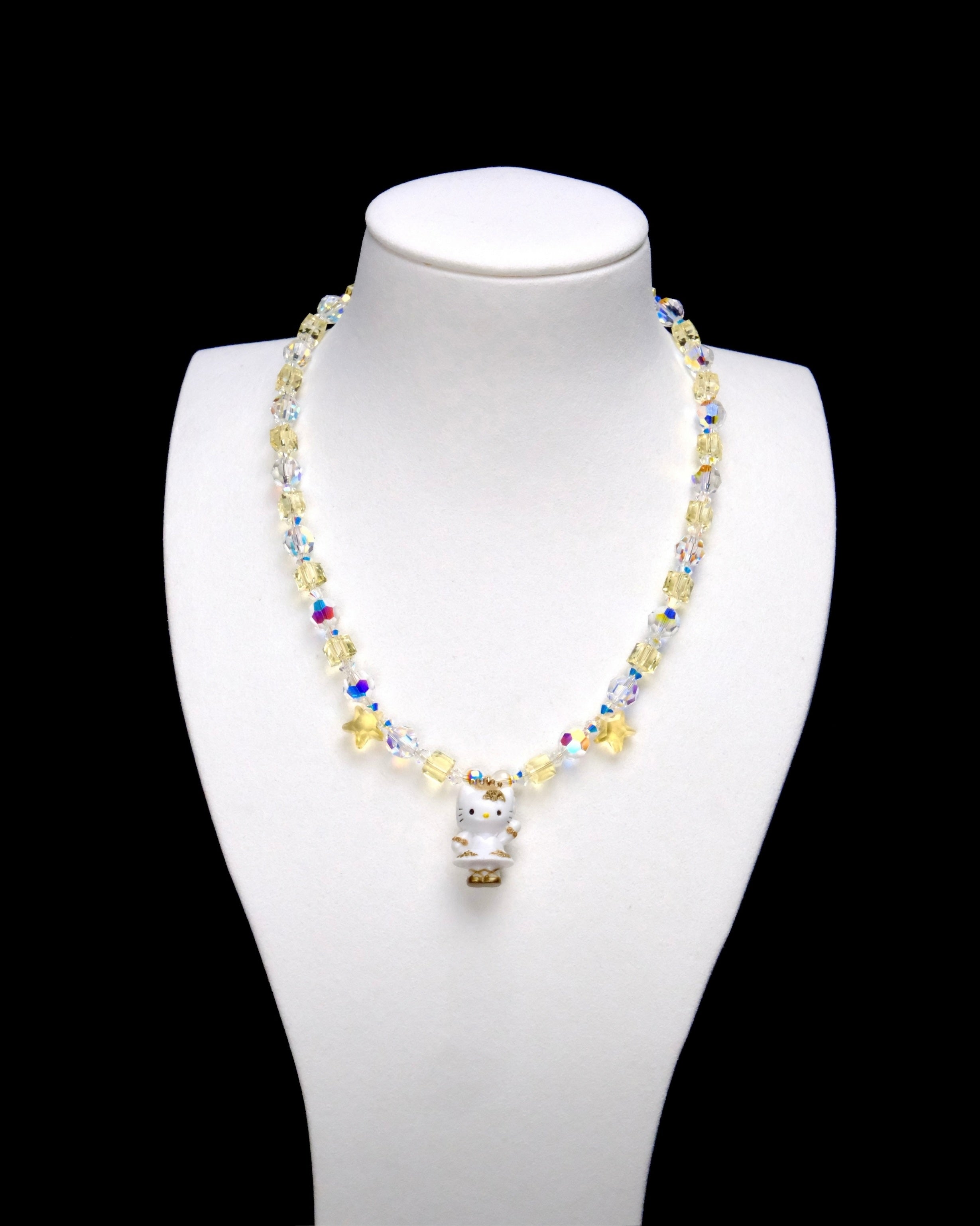 Pale yellow crystal cubes alternate with clear iridescent rounds. Two yellow stars frame a Hello Kitty charm in a white outfit with gold-colored details.