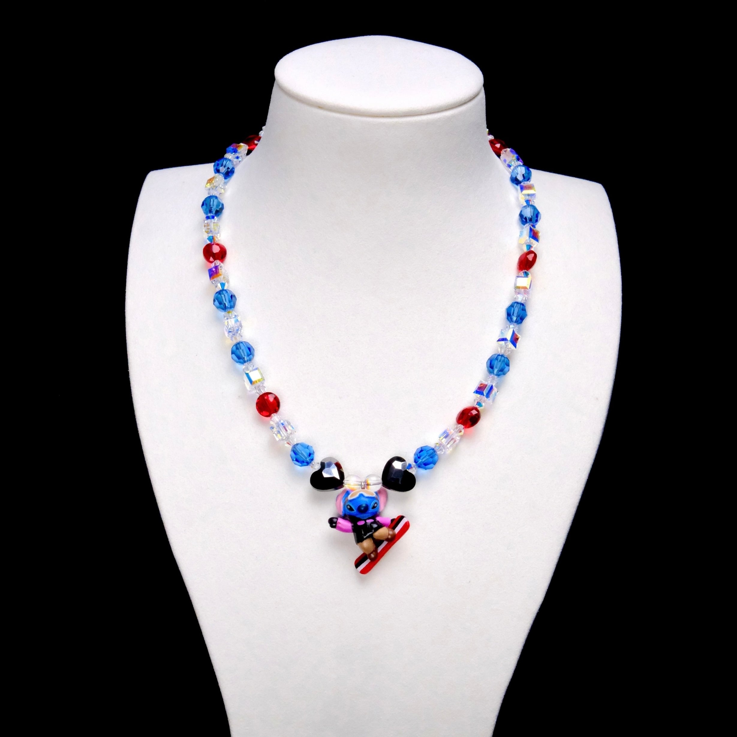 Blue and red crystal rounds, iridescent crystal cubes and two black heart accents surround a Stitch charm riding a red-and-white board.