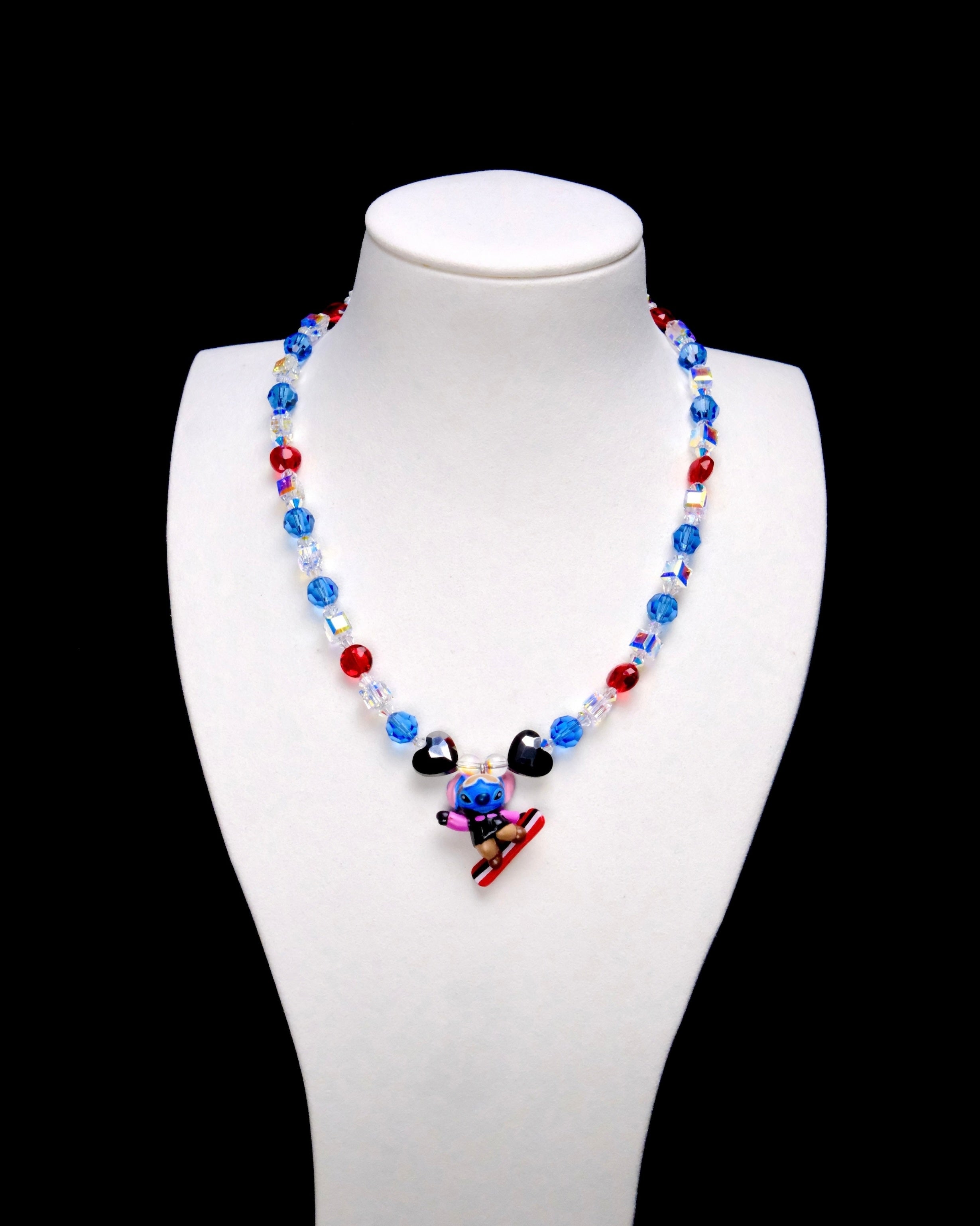 Blue and red crystal rounds, iridescent crystal cubes and two black heart accents surround a Stitch charm riding a red-and-white board.