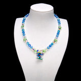 Blue crystal rounds and light green stars surround a Stitch charm with yellow goggles, a red scarf and a green board.