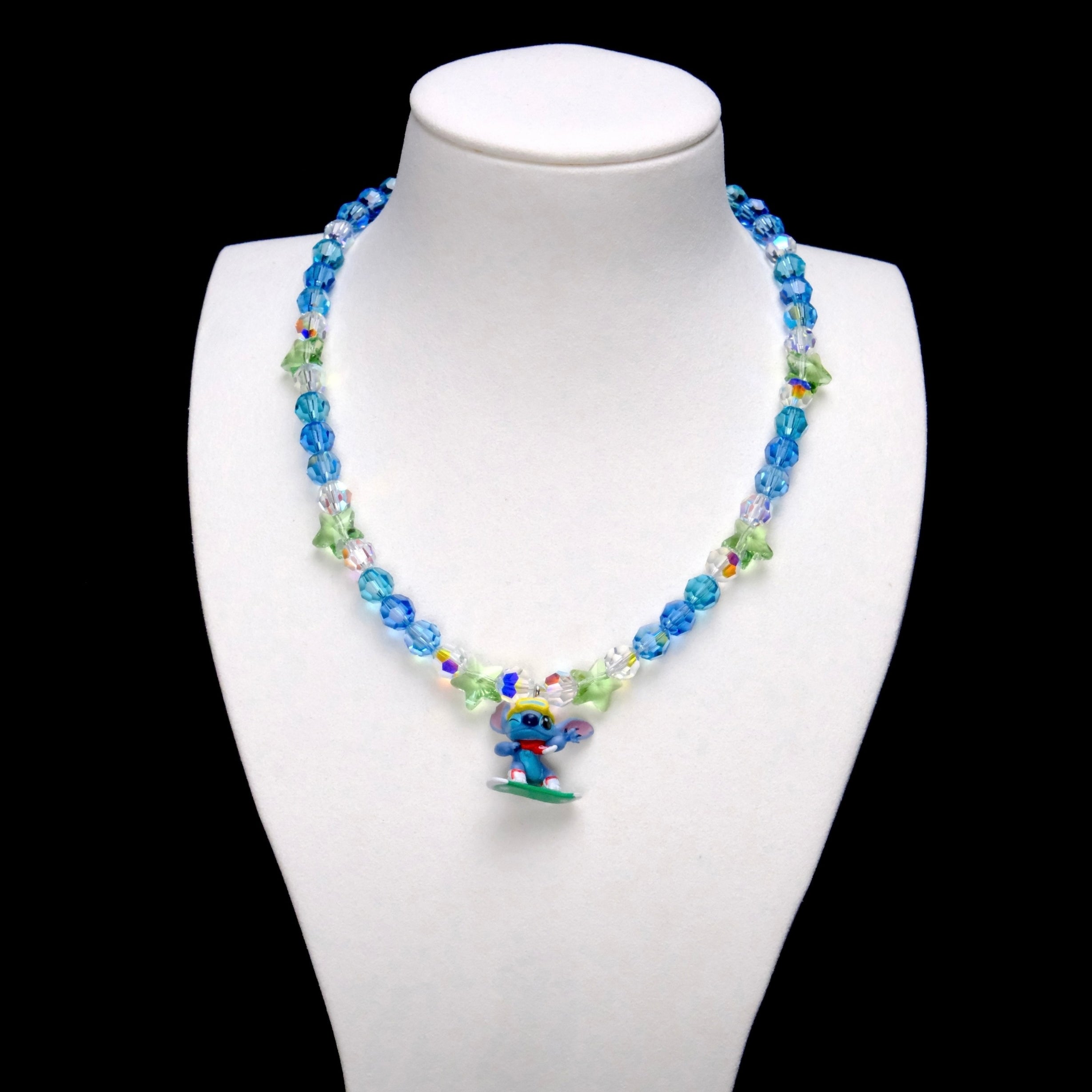 Blue crystal rounds and light green stars surround a Stitch charm with yellow goggles, a red scarf and a green board.