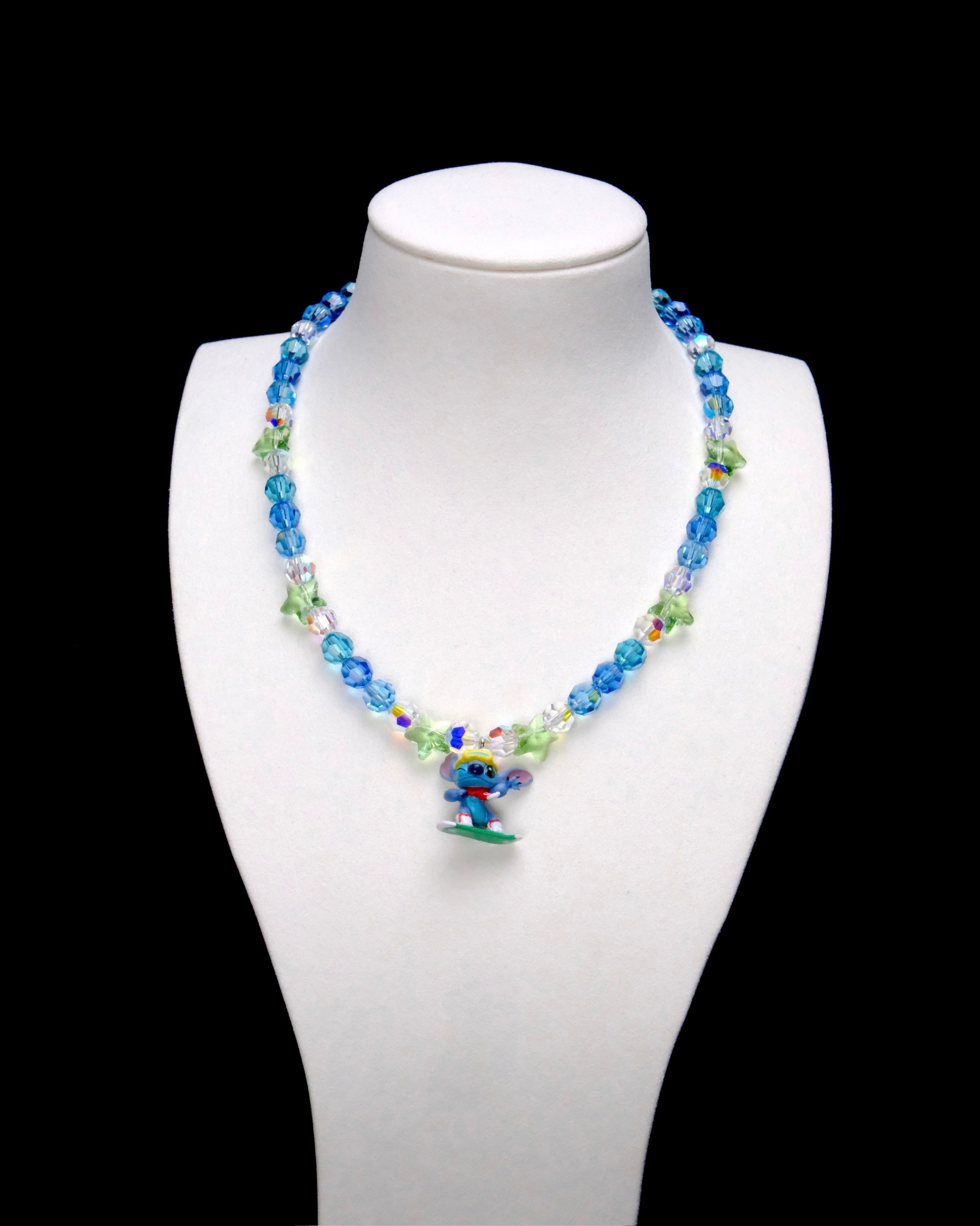 Blue crystal rounds and light green stars surround a Stitch charm with yellow goggles, a red scarf and a green board.