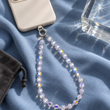 Aurora iridescent crystal phone chain attached to an ivory phone on blue fabric, showing rainbow reflections.