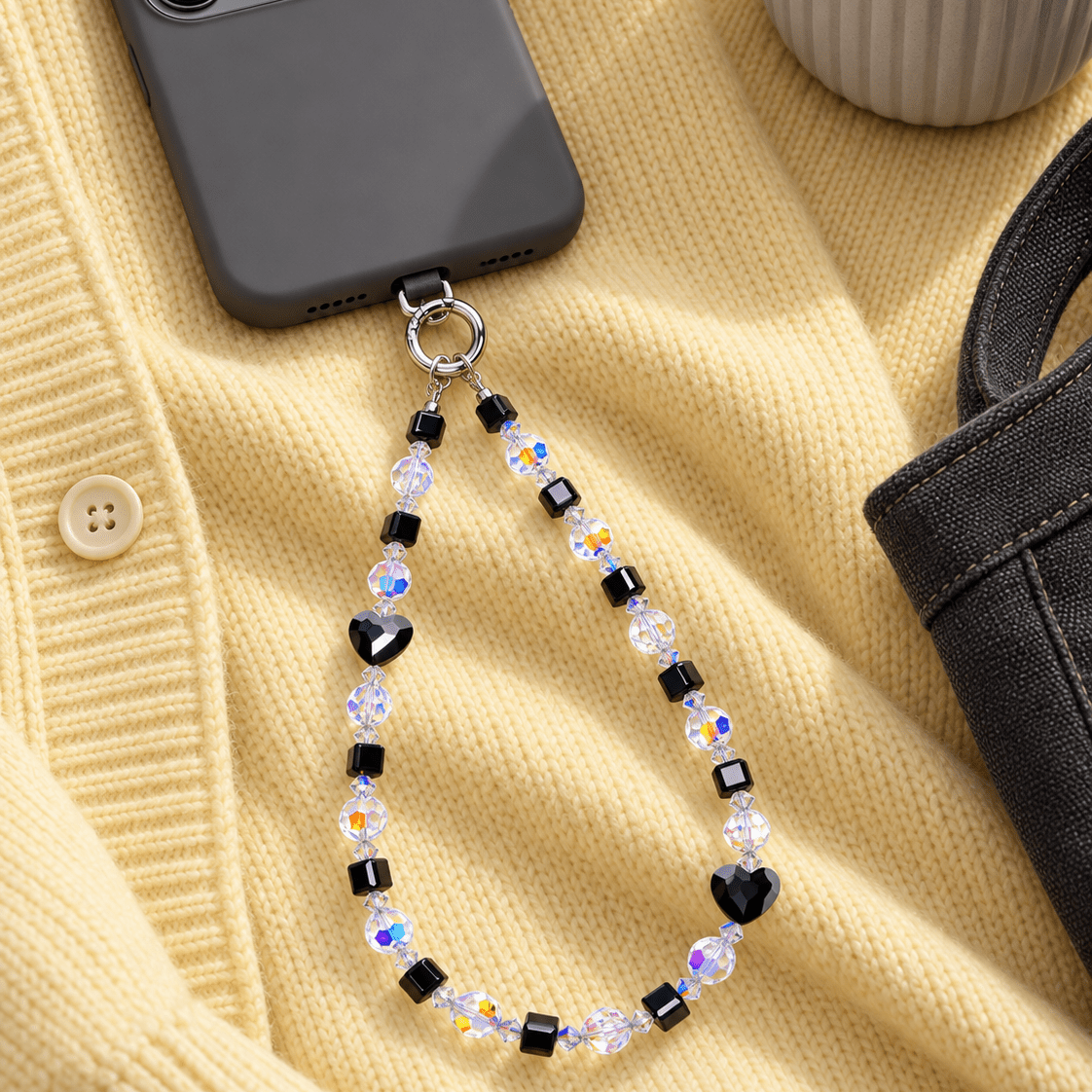 Black heart and cube crystal phone chain with iridescent beads, attached to a dark phone on yellow knit fabric.