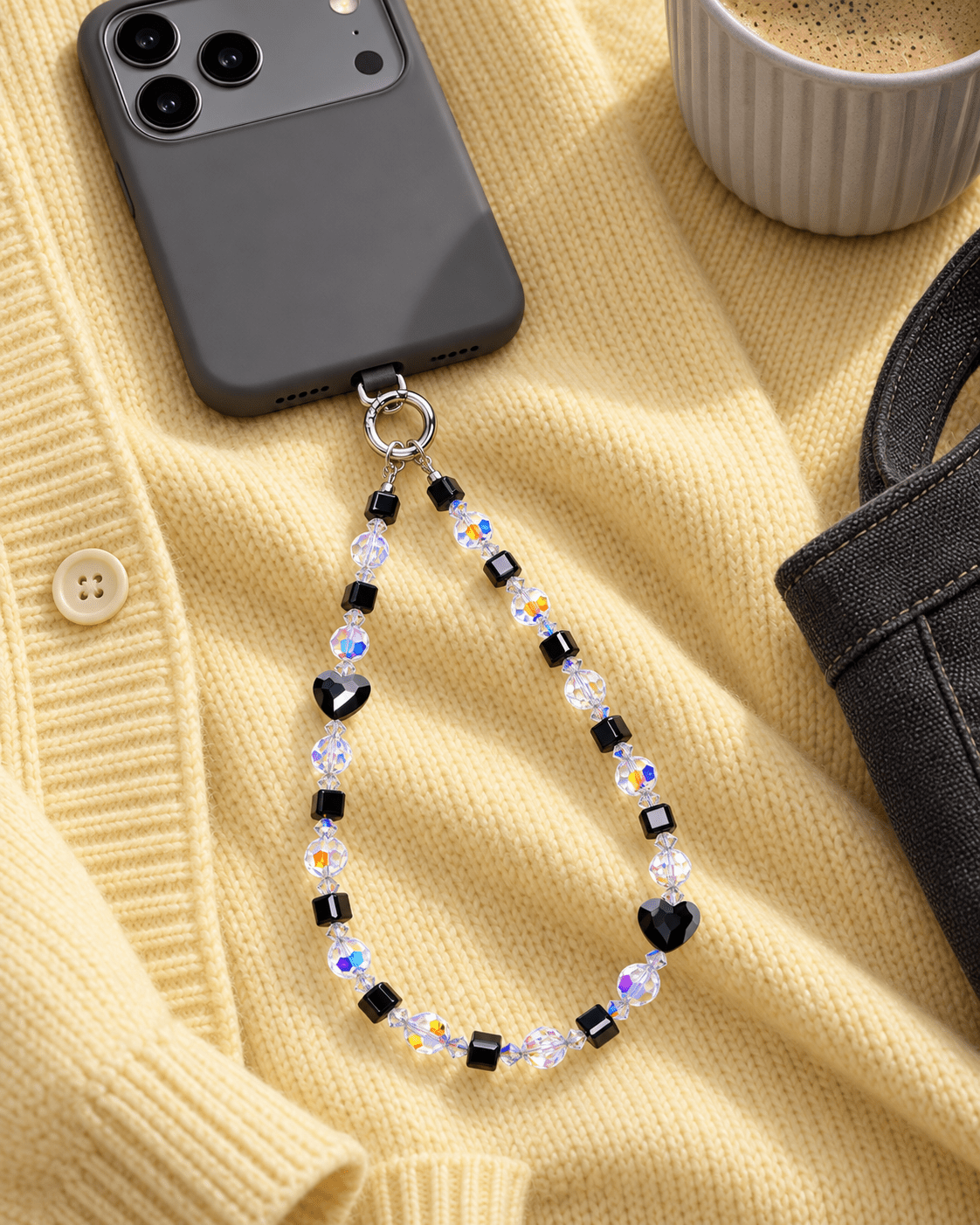 Black heart and cube crystal phone chain with iridescent beads, attached to a dark phone on yellow knit fabric.