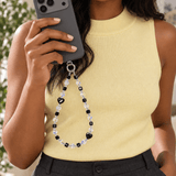 Woman in a yellow top holding a dark phone with a black heart and iridescent crystal phone chain.