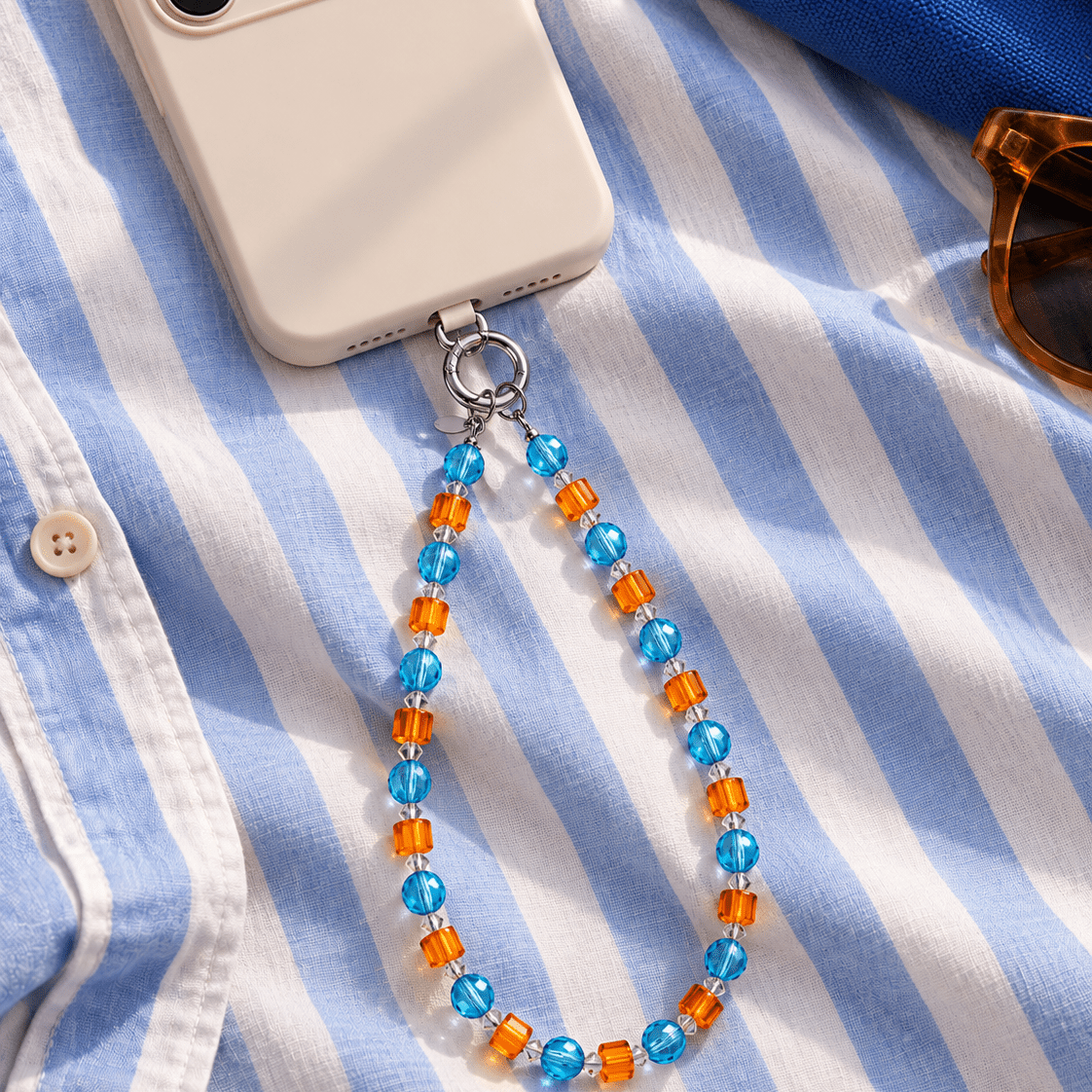 Blue and orange crystal phone chain attached to an ivory phone on blue and white striped fabric.