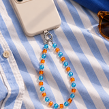 Blue and orange crystal phone chain attached to an ivory phone on blue and white striped fabric.