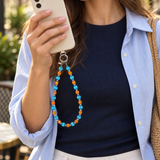 Woman in a blue shirt holding an ivory phone with a blue and orange crystal phone chain.