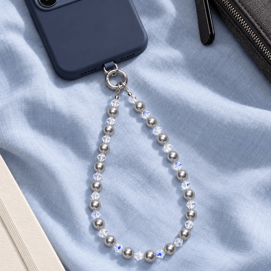 Gray pearl and clear crystal phone chain attached to a navy phone on pale blue fabric.