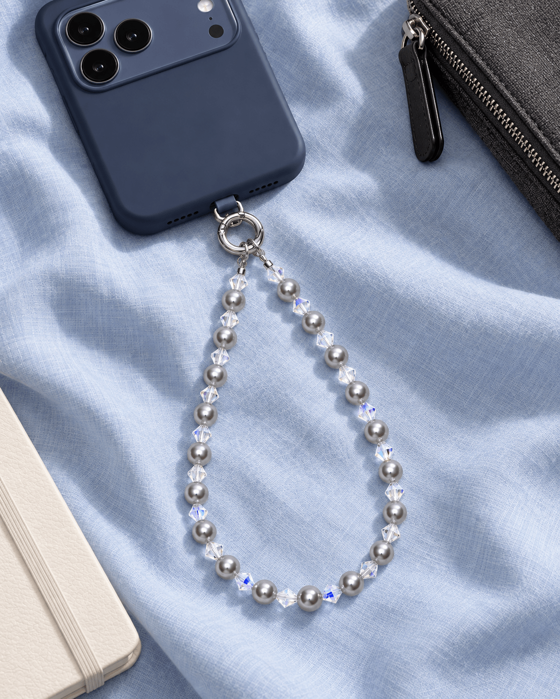 Gray pearl and clear crystal phone chain attached to a navy phone on pale blue fabric.
