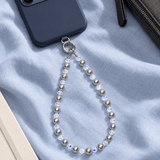 Gray pearl and clear crystal phone chain attached to a navy phone on pale blue fabric.