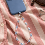 Pink and pale blue pearl-effect phone chain attached to a blue phone on pink and cream striped fabric.