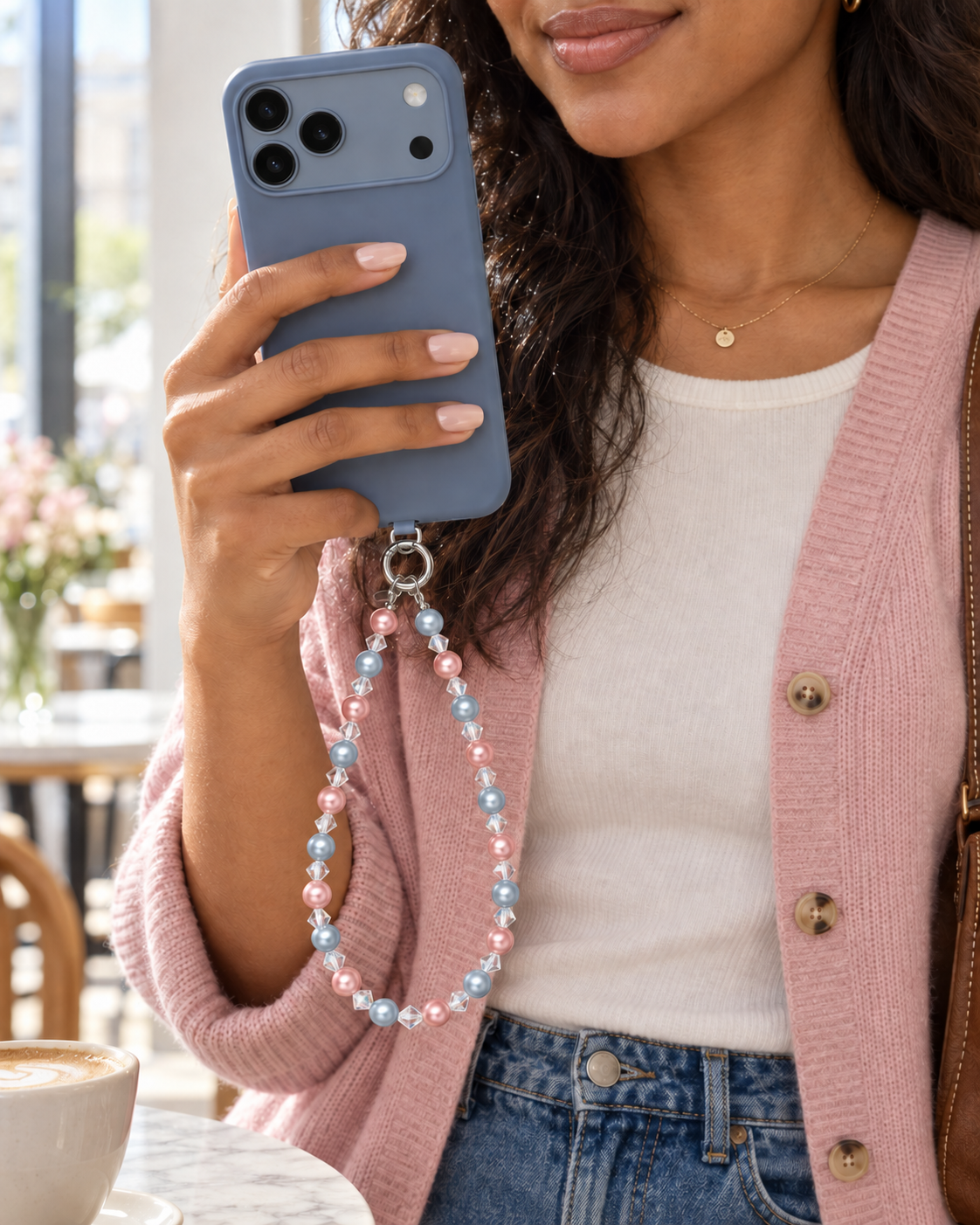 Woman in a pink cardigan holding a blue phone with a pink and pale blue pearl-effect phone chain.