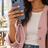 Woman in a pink cardigan holding a blue phone with a pink and pale blue pearl-effect phone chain.