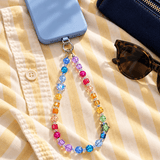Rainbow crystal phone chain with a blue heart and green star, attached to a blue phone on yellow striped fabric.