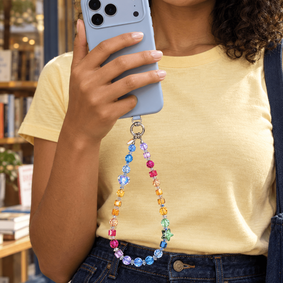 Woman in a yellow T-shirt holding a blue phone with a rainbow crystal phone chain.