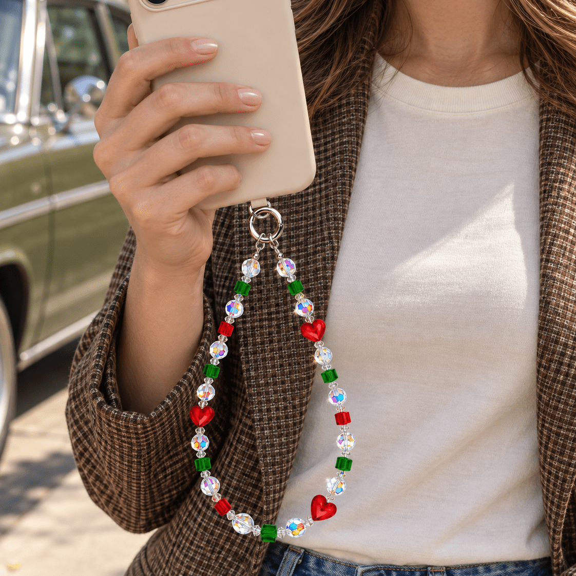 Woman in a brown blazer holding an ivory phone with a red heart and green crystal phone chain.