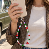 Woman in a brown blazer holding an ivory phone with a red heart and green crystal phone chain.