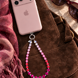 Rose ombre crystal phone chain with pale pink, pink, red and plum beads, attached to a pink phone on a brown bag.