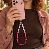 Rose ombre crystal phone chain hanging from a pink phone held by a woman in a dusty pink jacket.