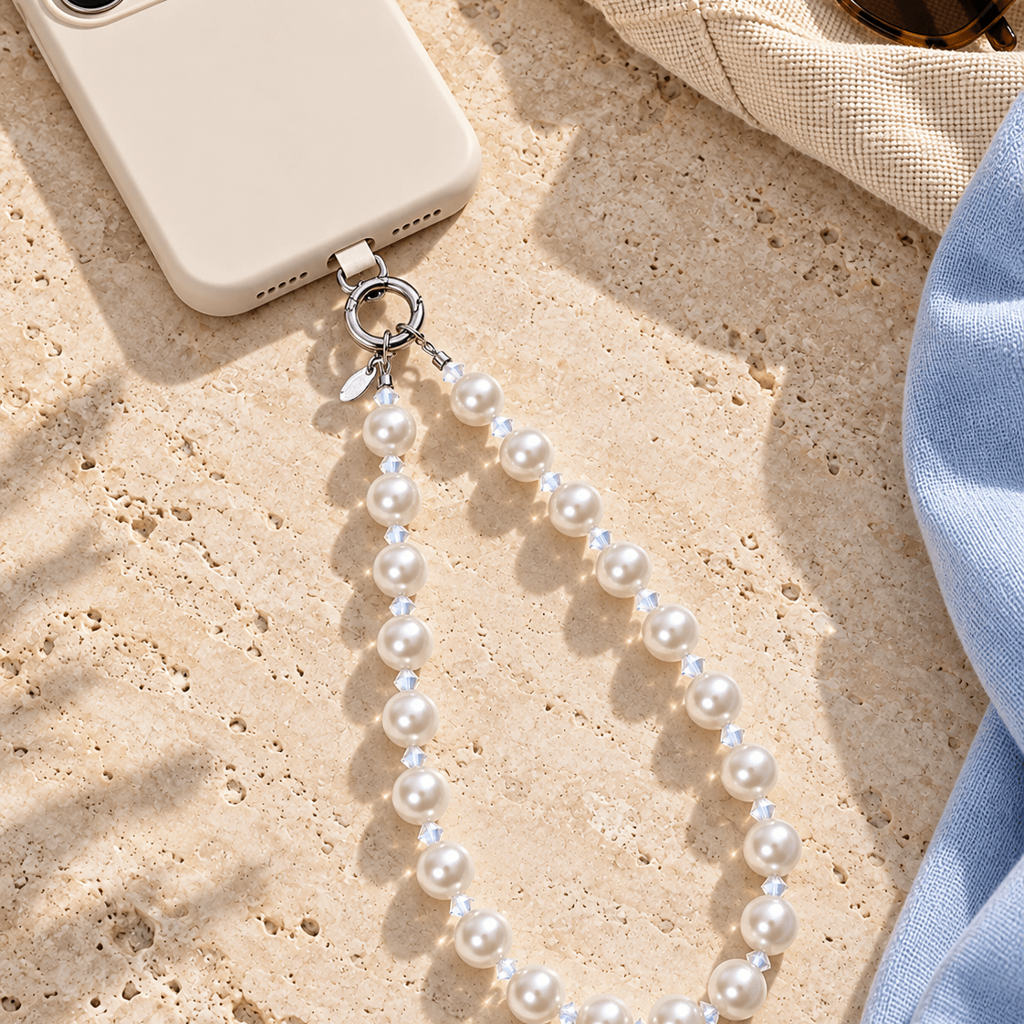 White pearl and clear crystal phone chain attached to an ivory phone on a light stone surface.